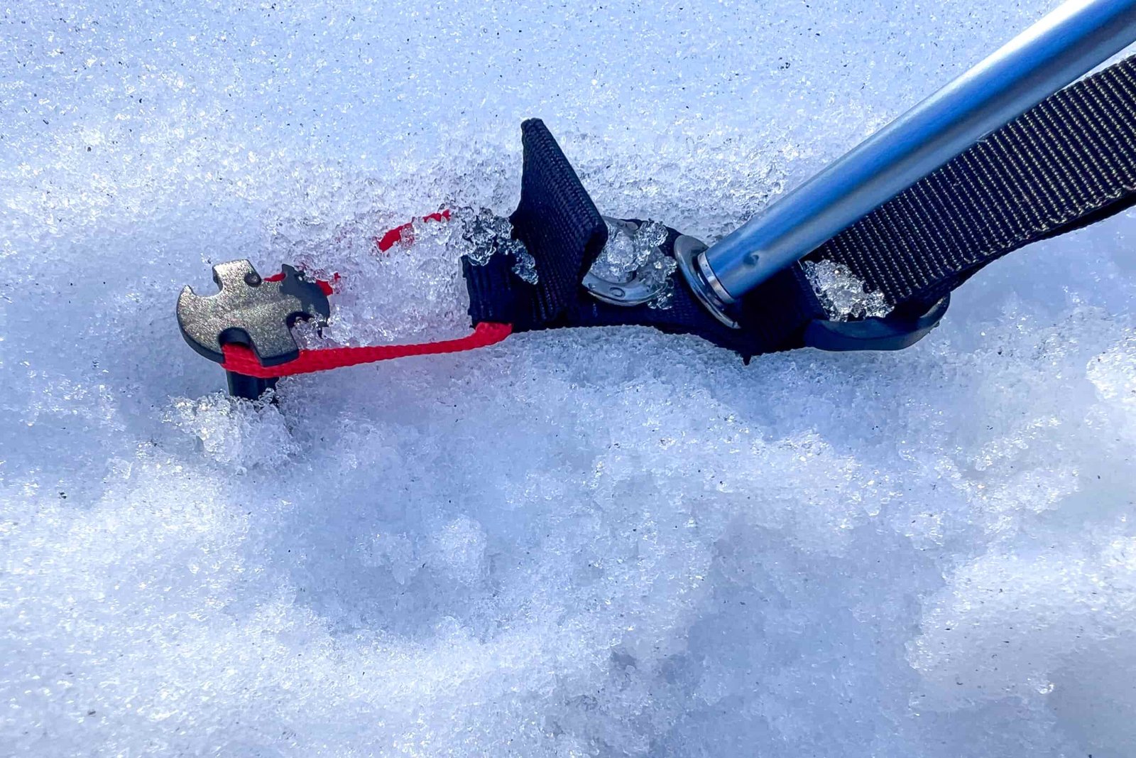 A close-up of a stake loop for the Samaya 2.0 tent, buried in snow and securely fastened to an aluminum pole for added stability.