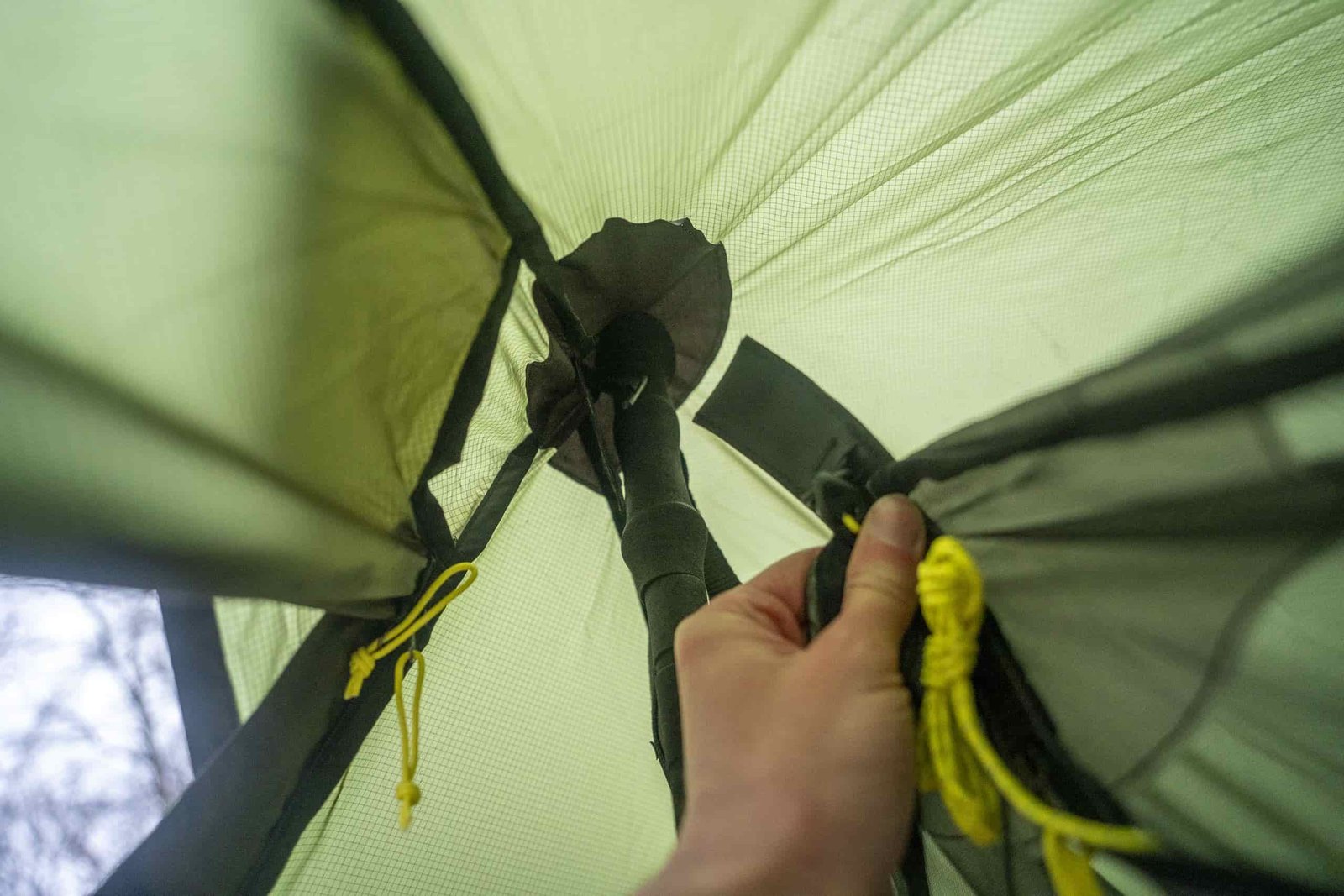 A hand holds and Internet tent towards the peak of a tarp