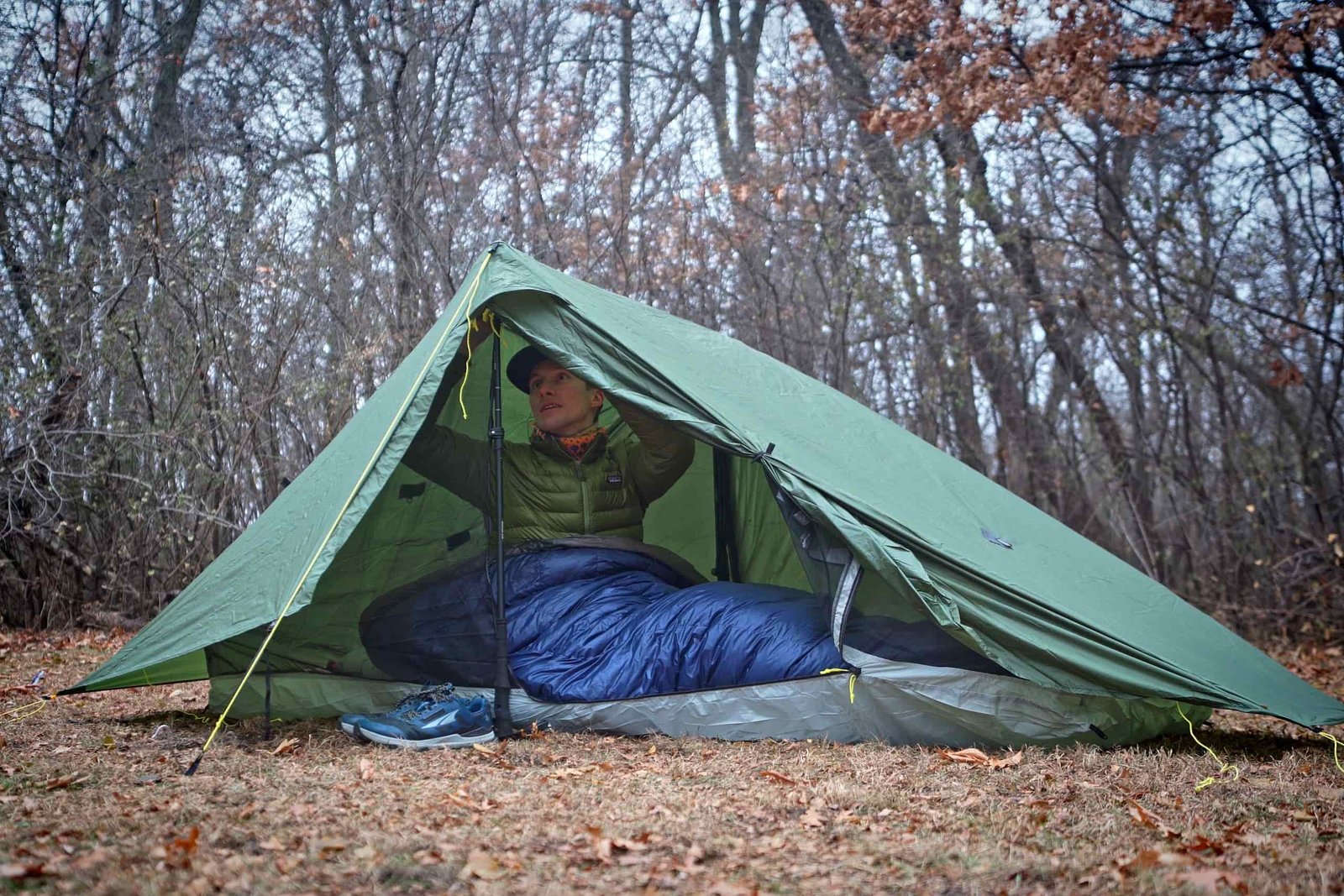 A man in a green jacket sits up in a green tent