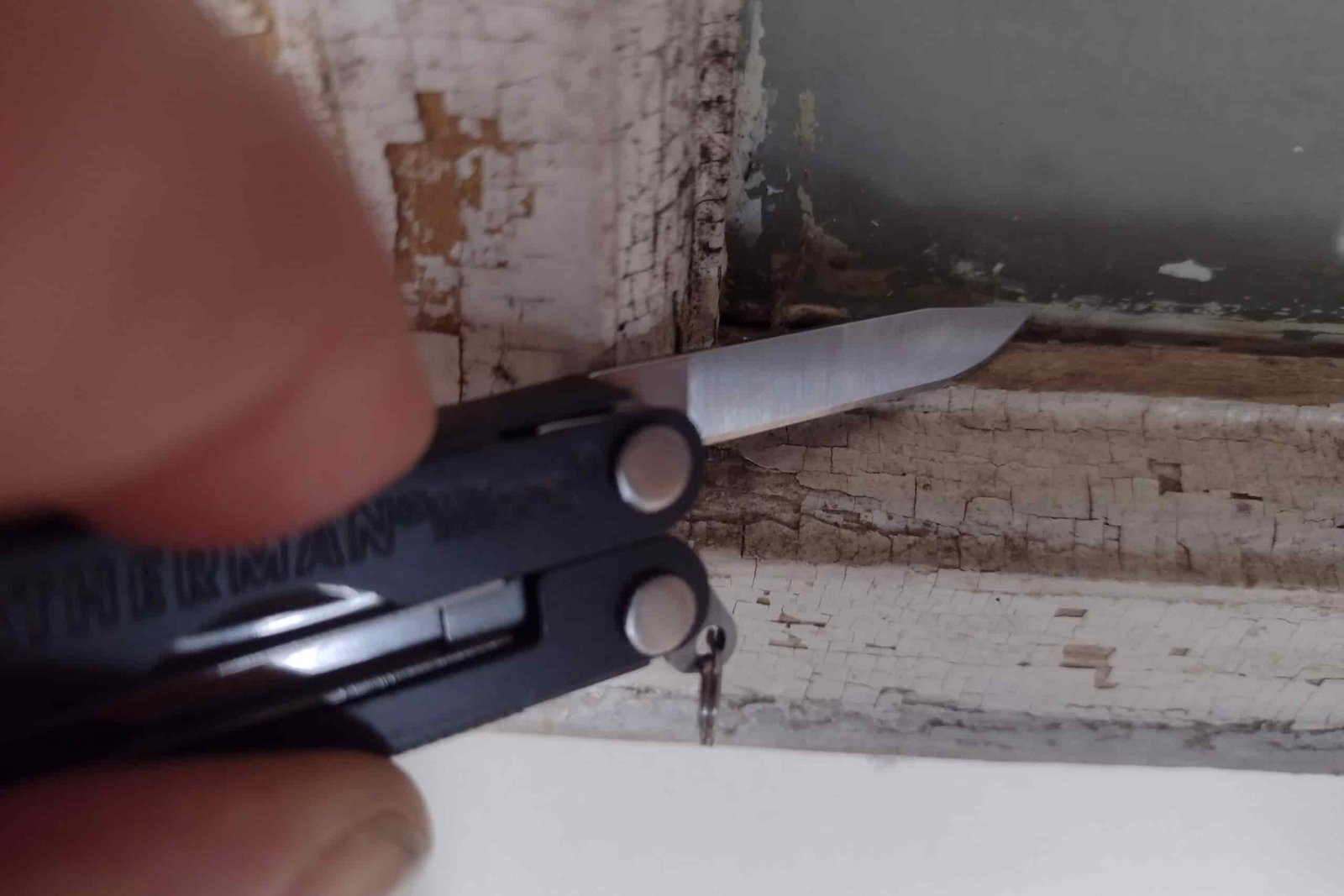 The Leatherman Micra with its blade scraping old paint from a window frame.