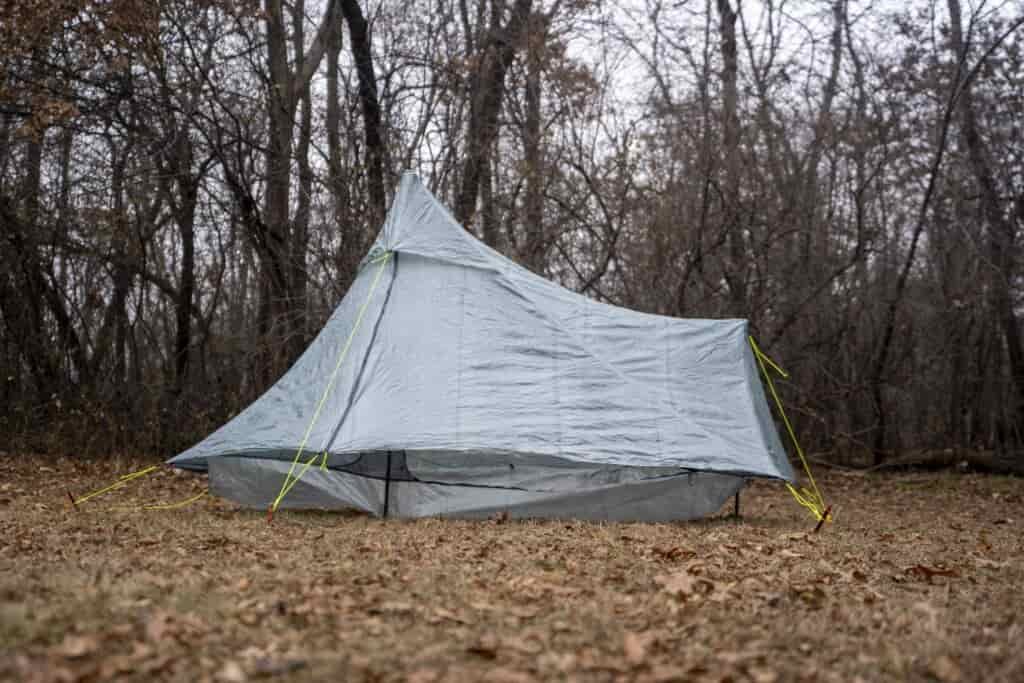 a silver green tent in a forest clearing