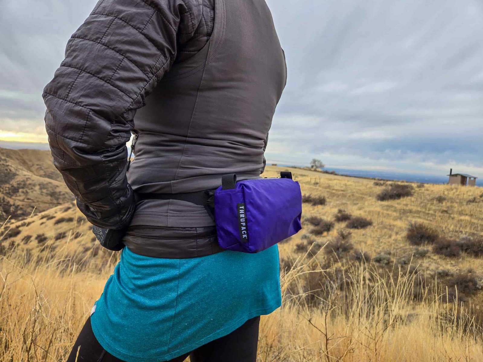 woman wearing the summit bum on her back on a hike through a high desert landscape in the fall or winter on a cloudy day