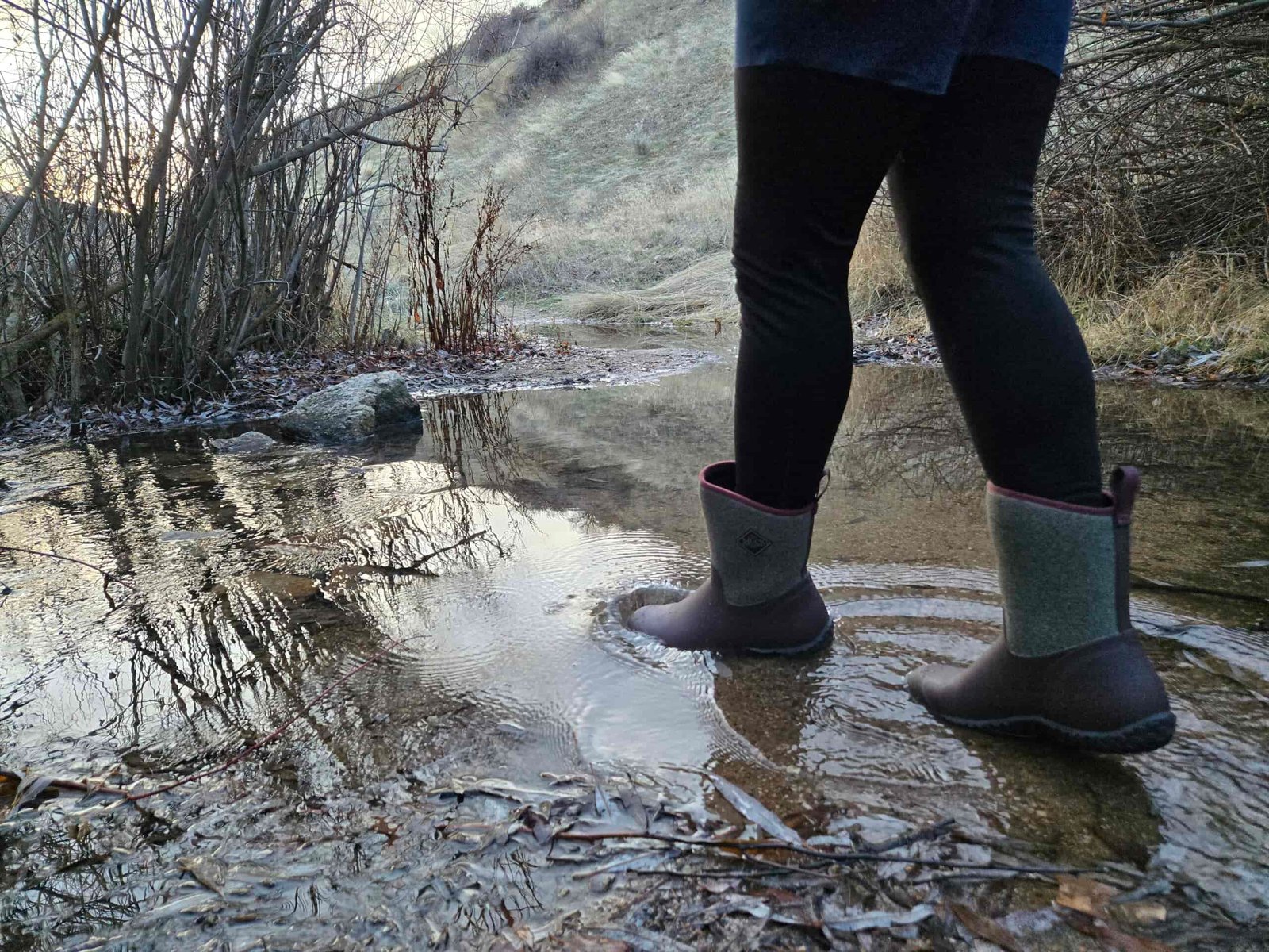woman walking in a creek wearing muck boots