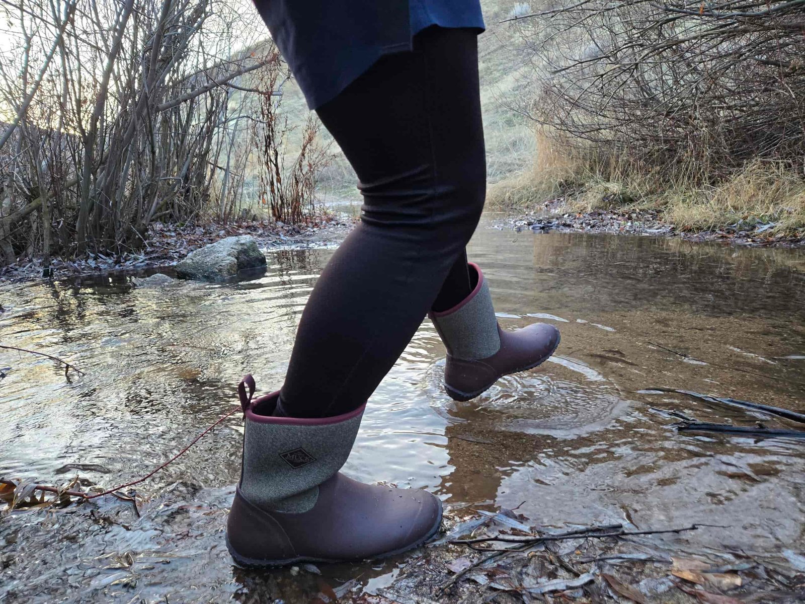 person walking across a creek in muck boots mucksters mid II