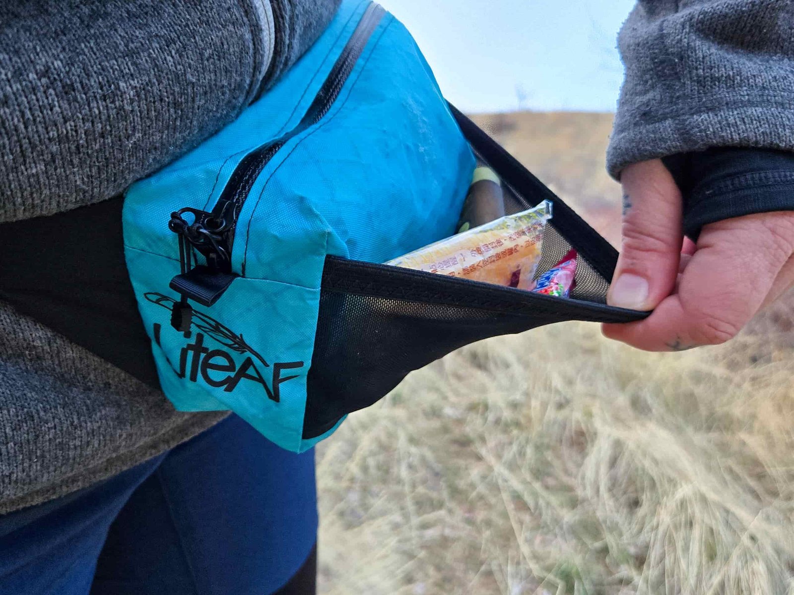 a hand pulling on the stretch pouch to show snacks being stored in the external pocket