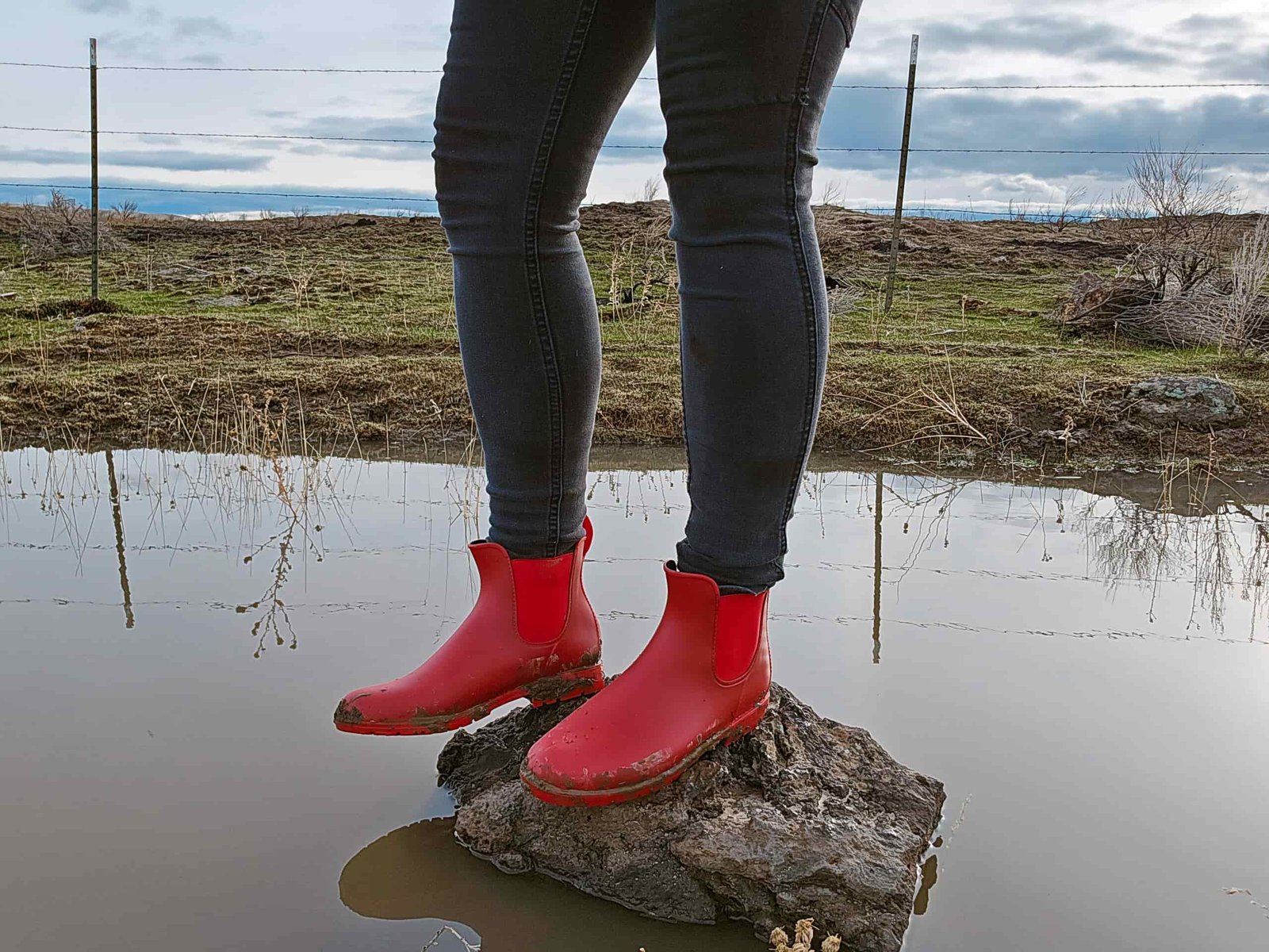 woman standing on a small rock surrounded by water. she's wearing the asgard chelsea boots
