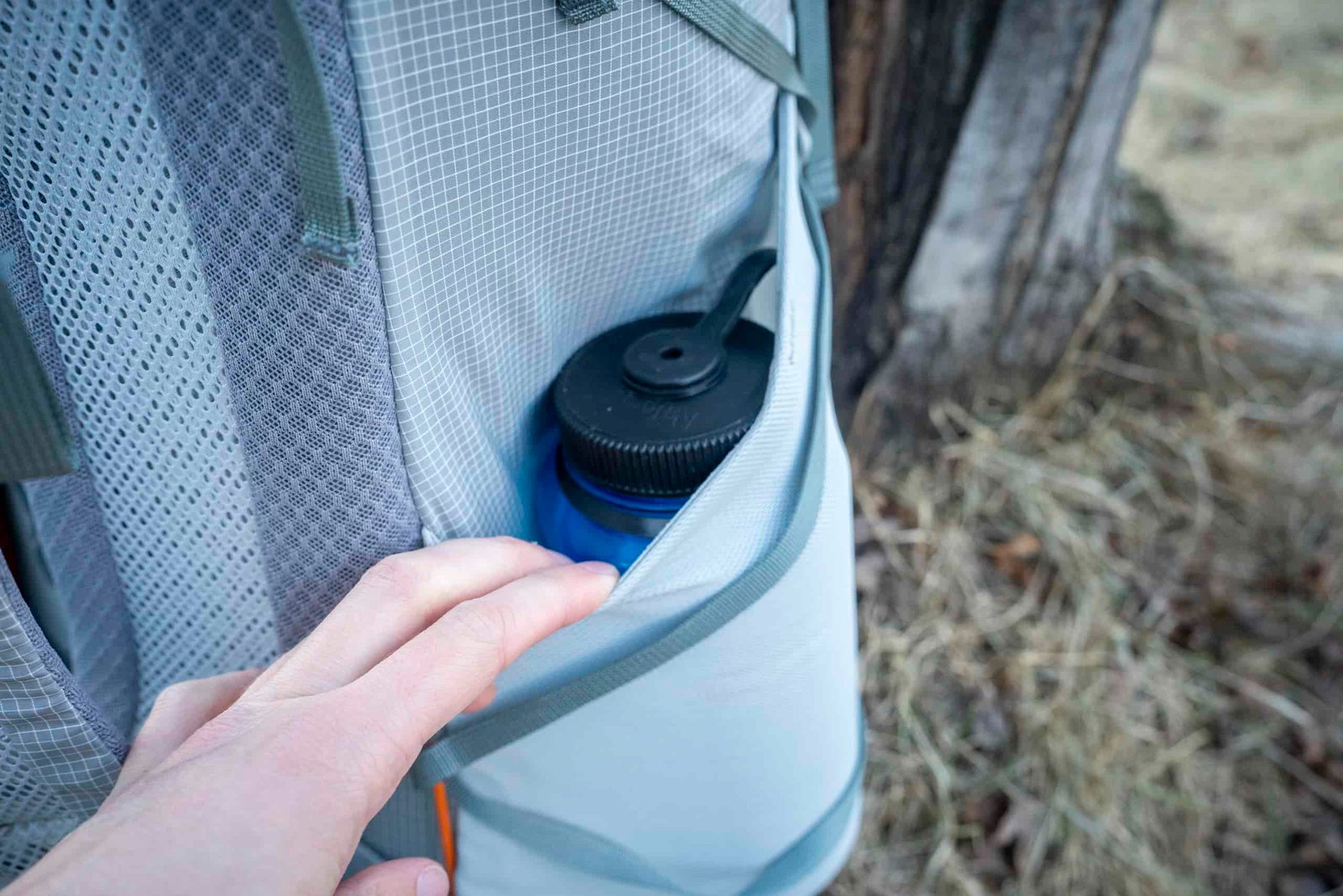 a hand holding open a backpack water bottle pocket