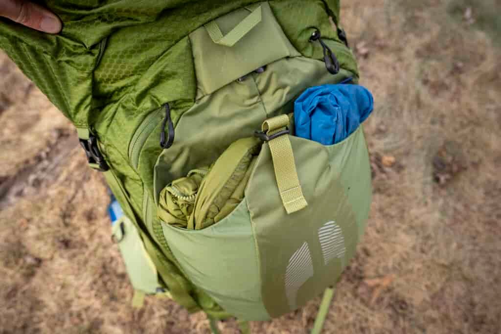 a rain jacket and puffy jacket stuffed in backpack pocket