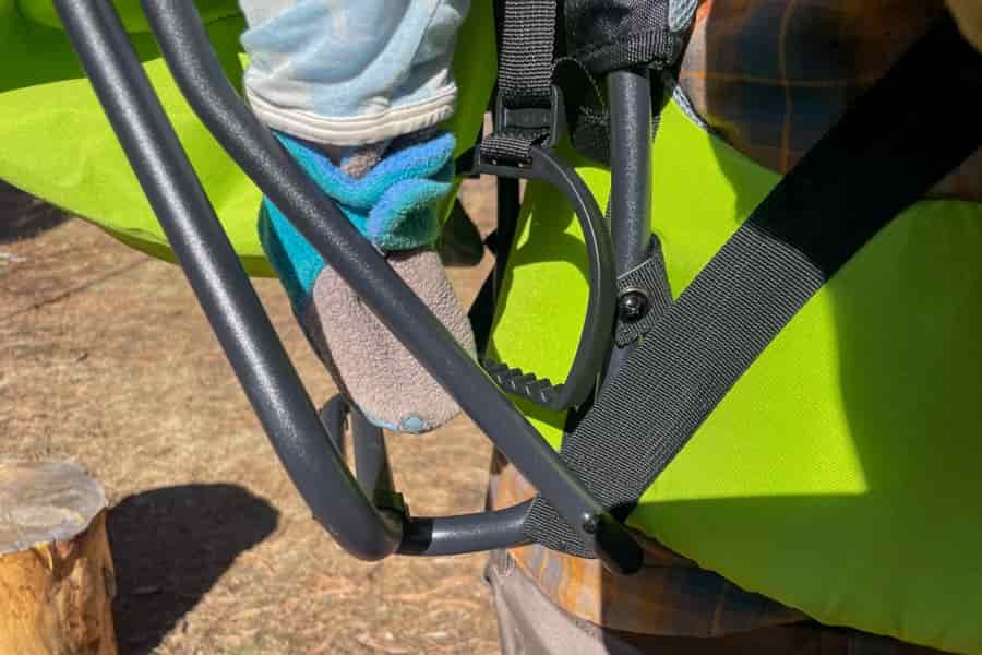 Close-up of a child's foot resting in the foot stirrup of a bright green child carrier.