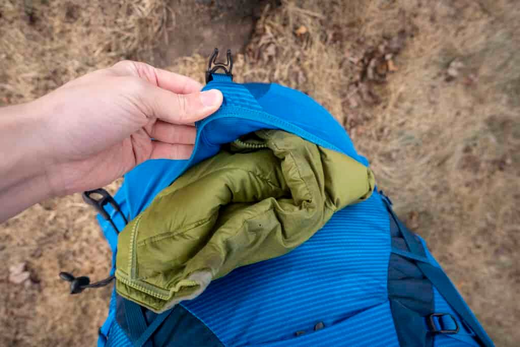 a hand holds a jacket stuffed in a backpack pocket