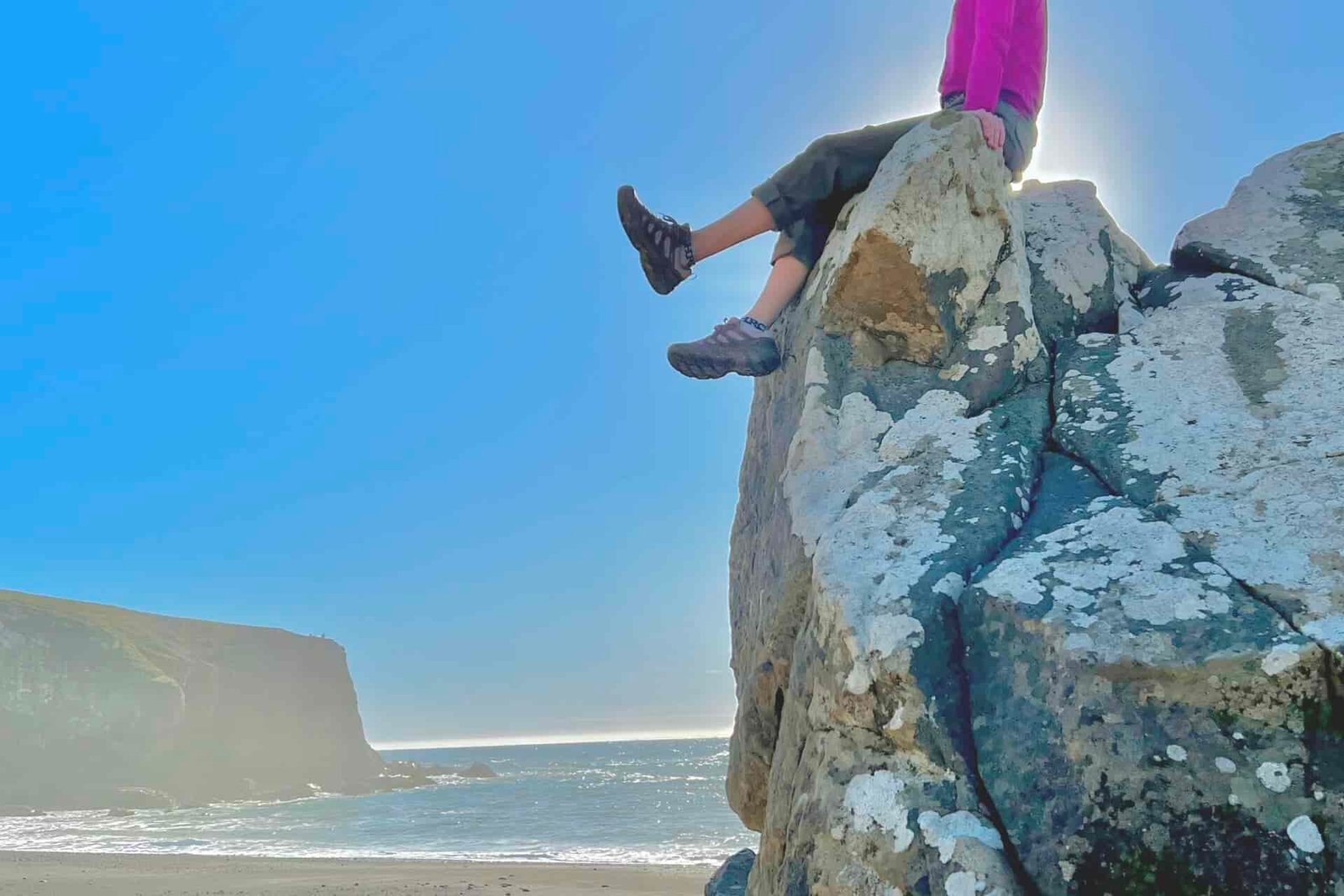 Women sitting on top of a large boulder with the beach in the background.