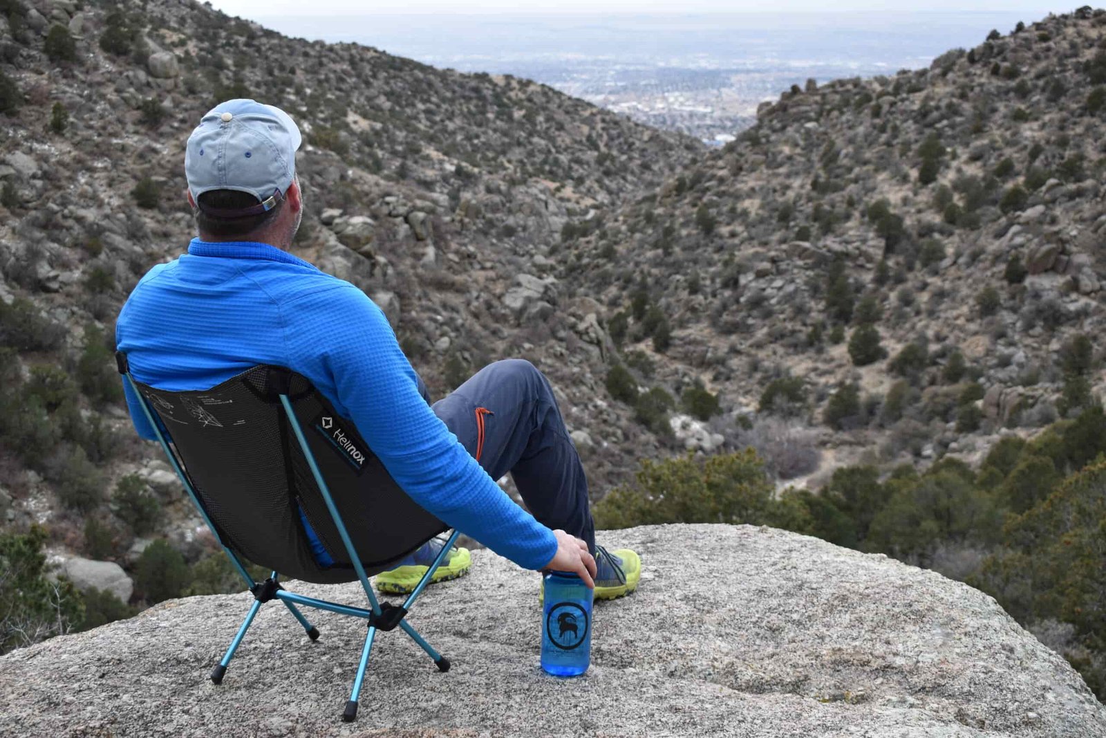 A hiker sits on the Helinox Chair Zero on a rocky cliff looking down a desert canyon