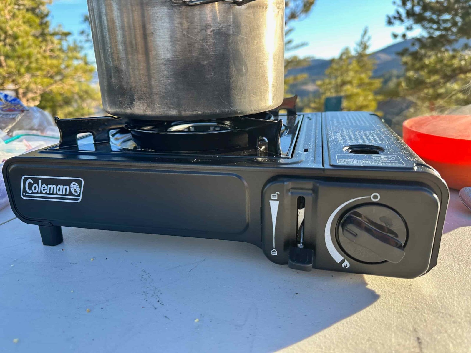 The Coleman Classic 1-Burner Butane Camping Stove cooking various meals at a campsite within the pines