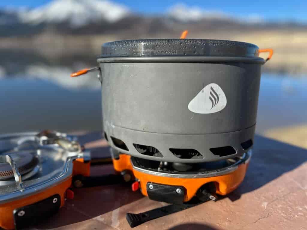 Jetboil Genesis Basecamp System at a lakeside campsite with a snowy mountain in the background