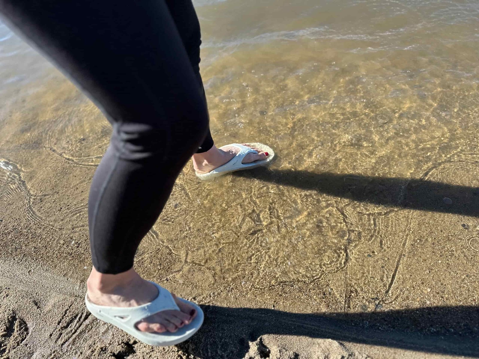 the OOfos OOriginals shoe splashing in water at a sandy lakeshore