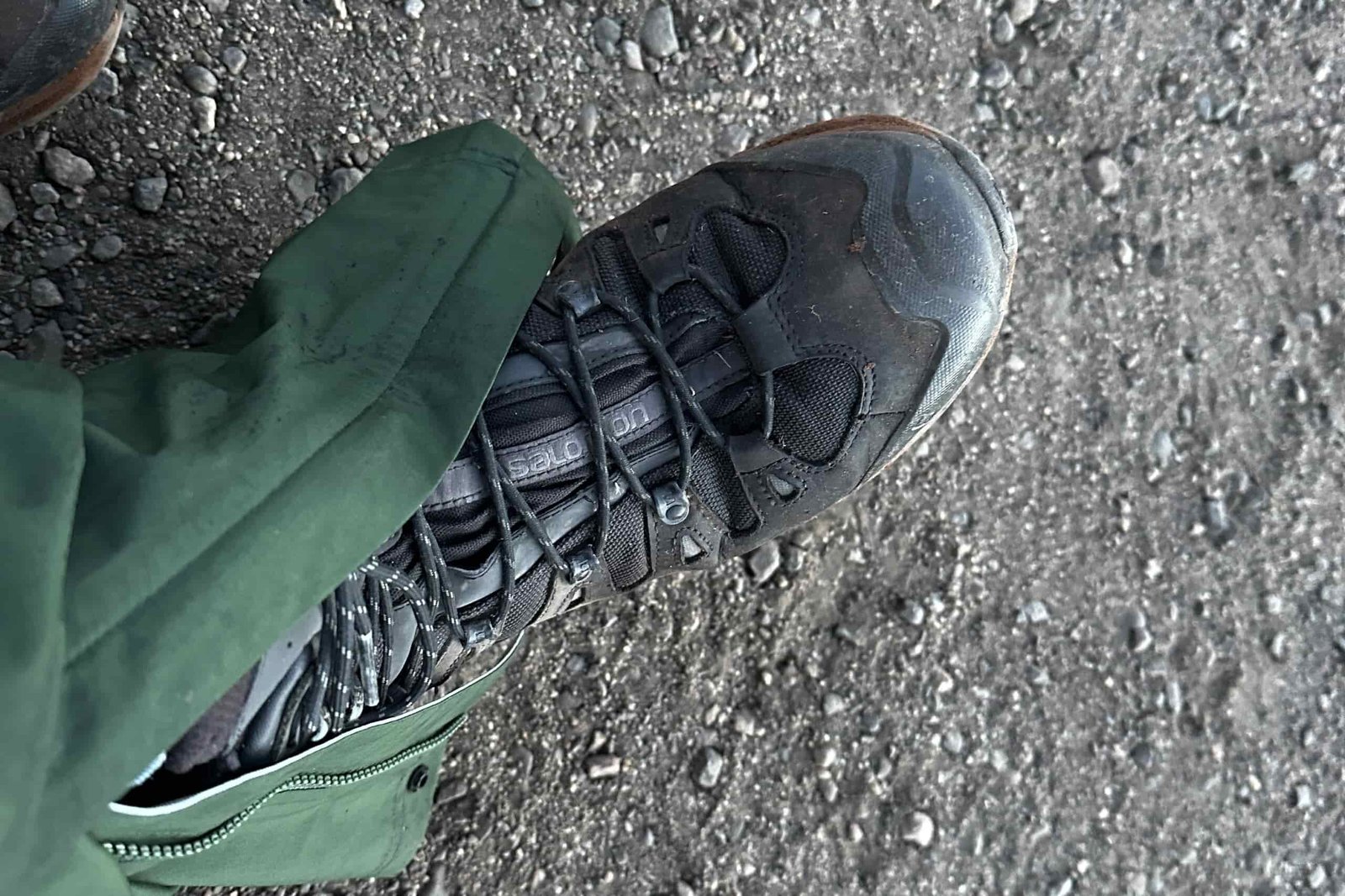Closeup of the ankle zipper area of the green REI Trailmade rain pants around a boot.