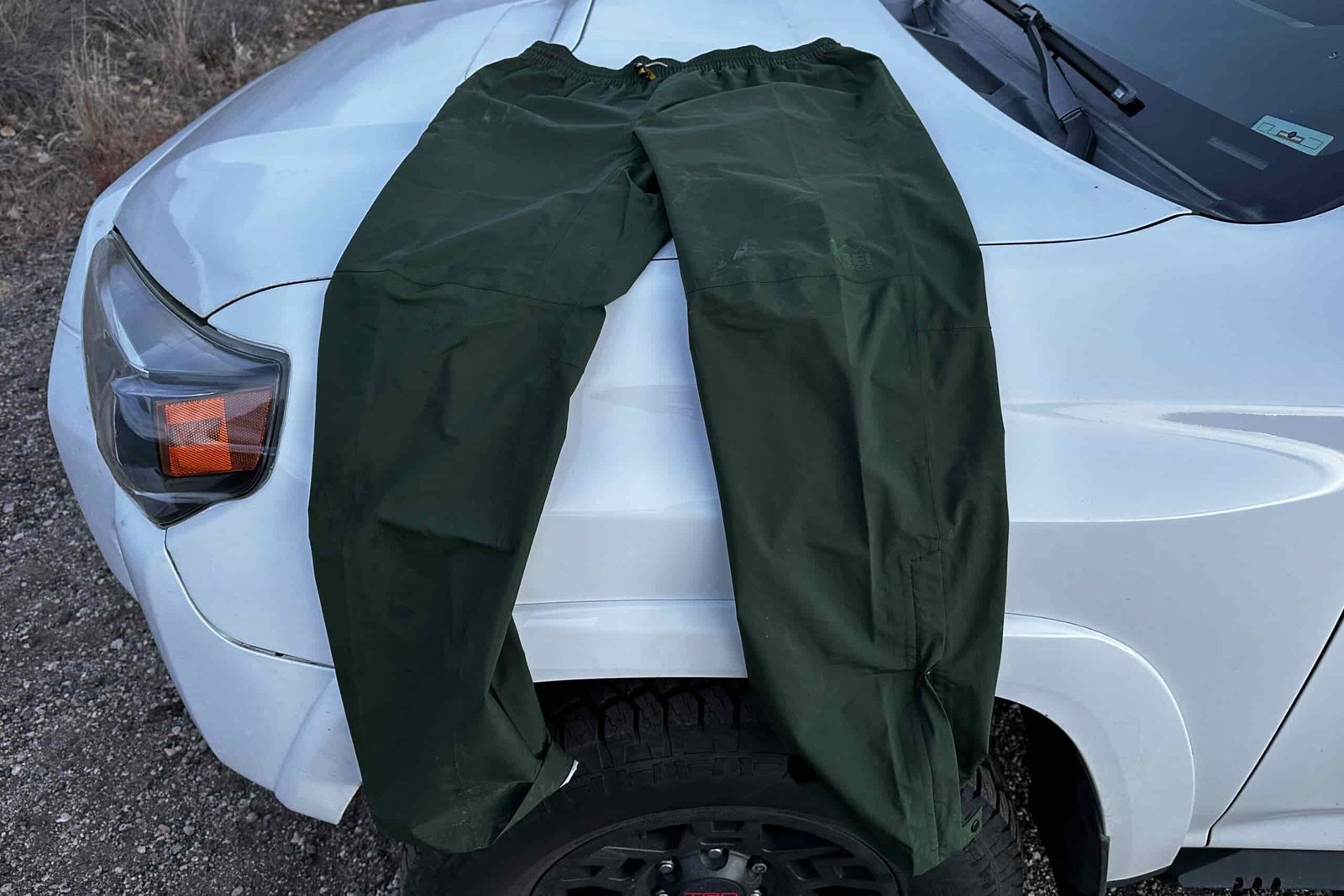 Closeup of the green REI Trailmade rain pants draped on a car hood.