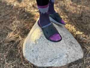 a woman wears the HOKA ORA Recovery 3 Slides while standing on a rock