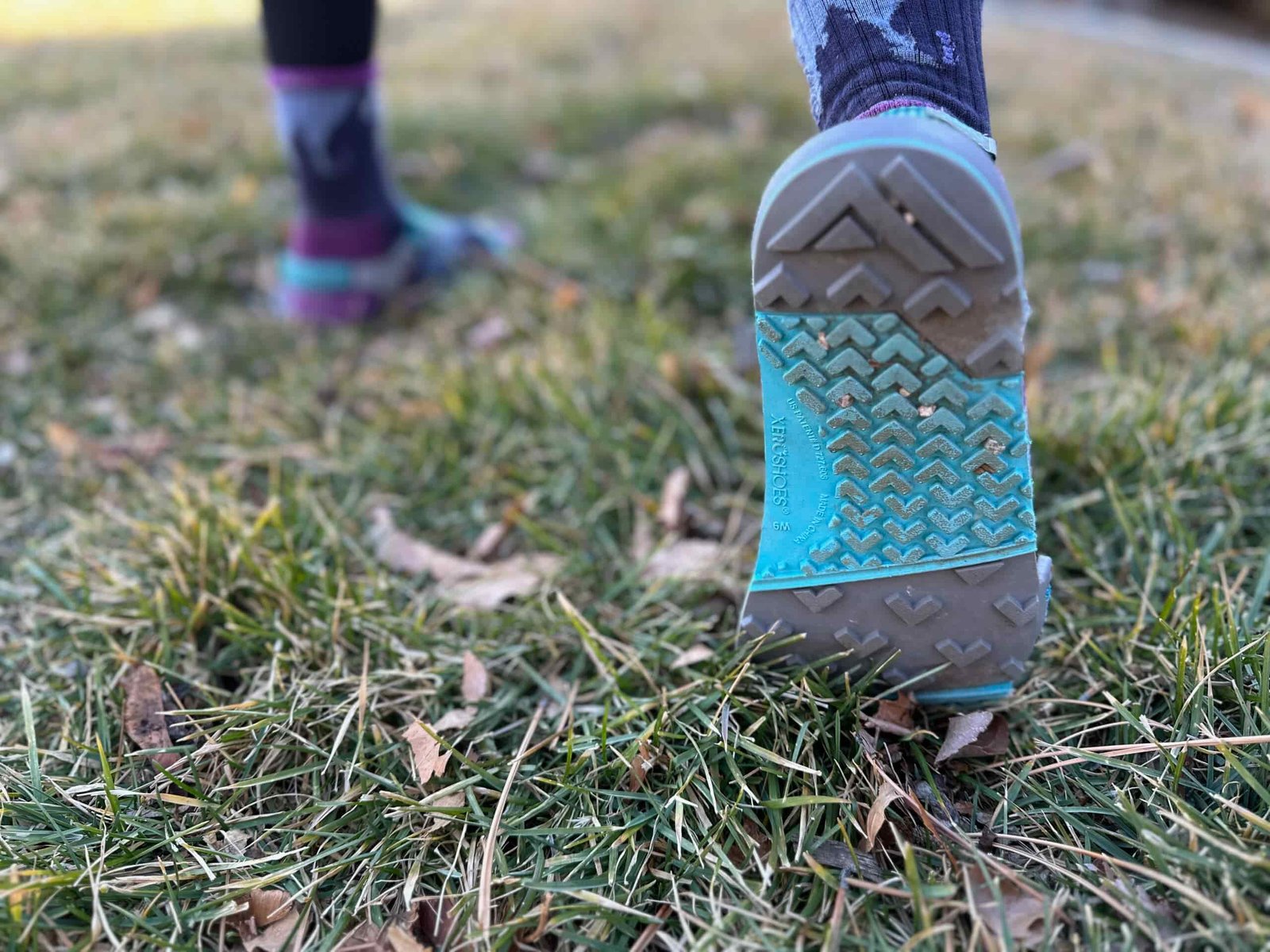 a woman shows off the soles of the Xero Shoes Z-Trail EV on grass