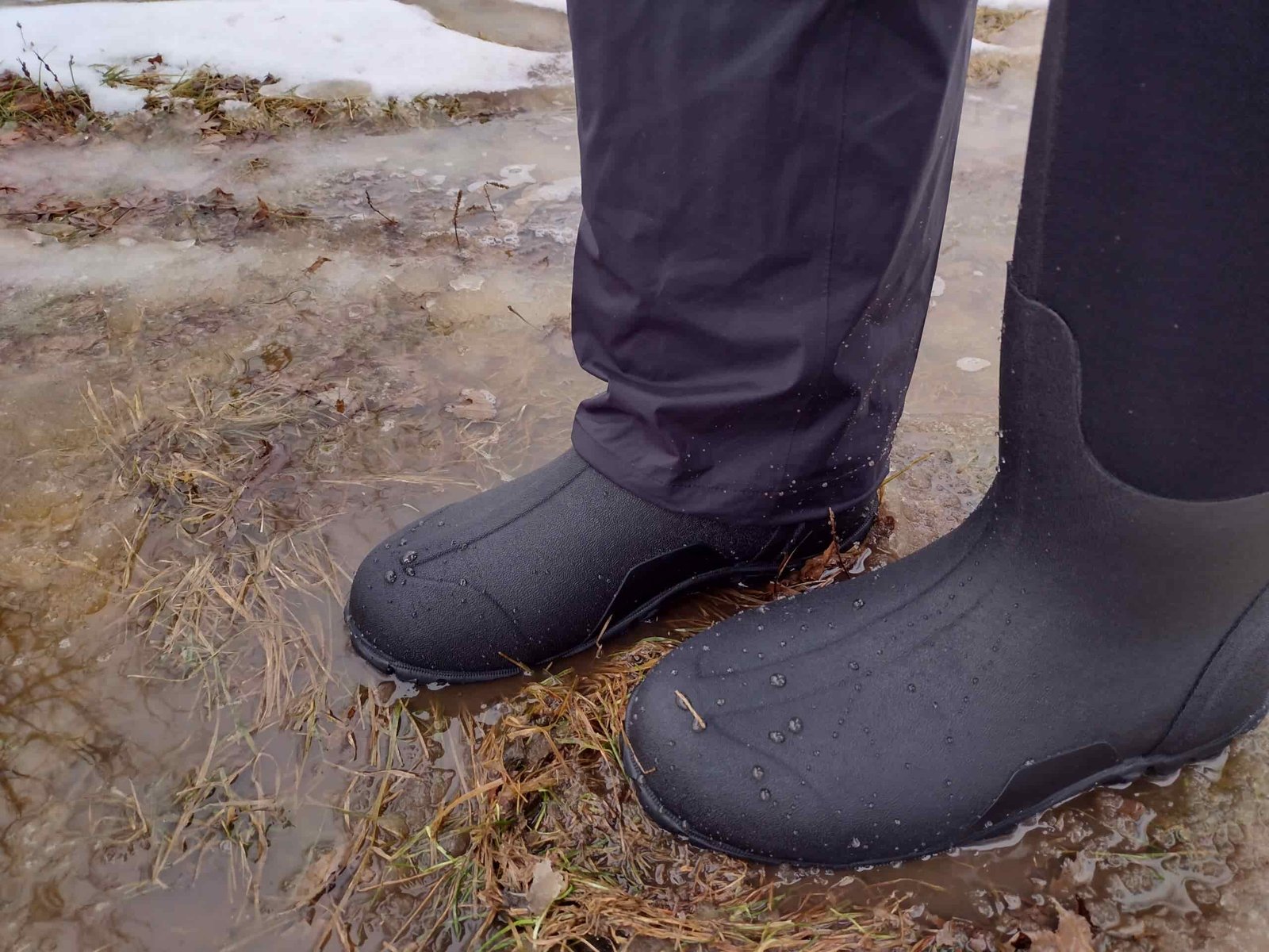 Ground level view of someone wearing the black Bogs Classic High standing on soggy ground.