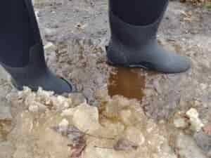 Ground level view of someone wearing the black Bogs Classic High standing in icy water.