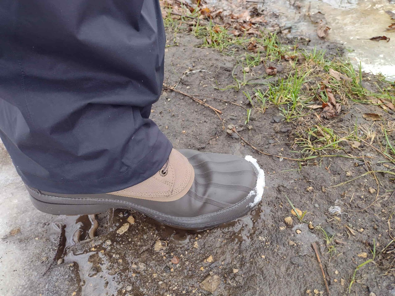 Ground level view of someone wearing the brown Sperry Cold Bay Chukka on mud and ice.