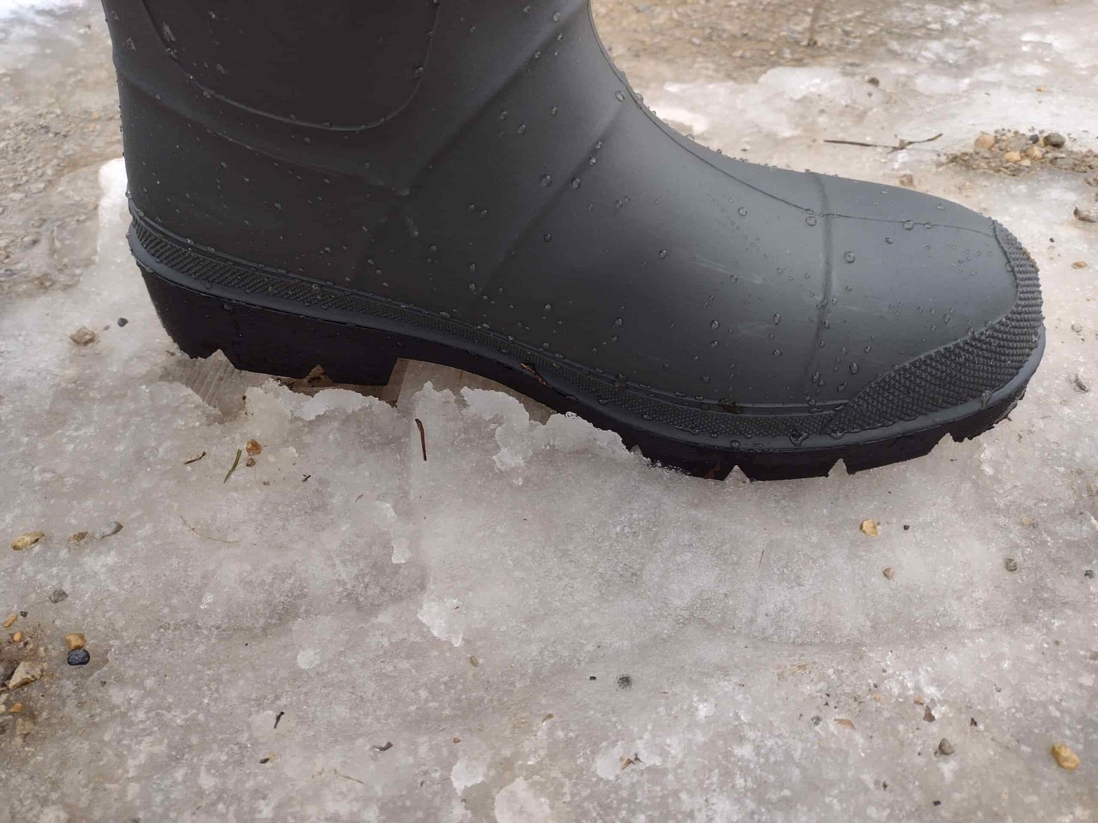 Ground level view of someone wearing the green Kamik Forester on icy slush.