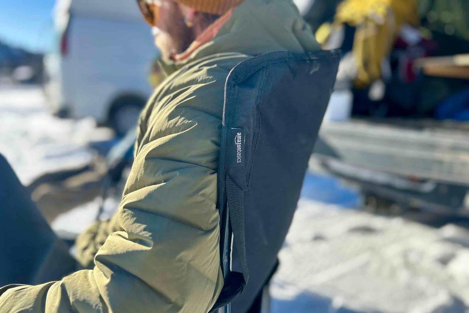 Close up side profile of the back of a camping chair with a person sitting in it, the logo visible on a small tag.