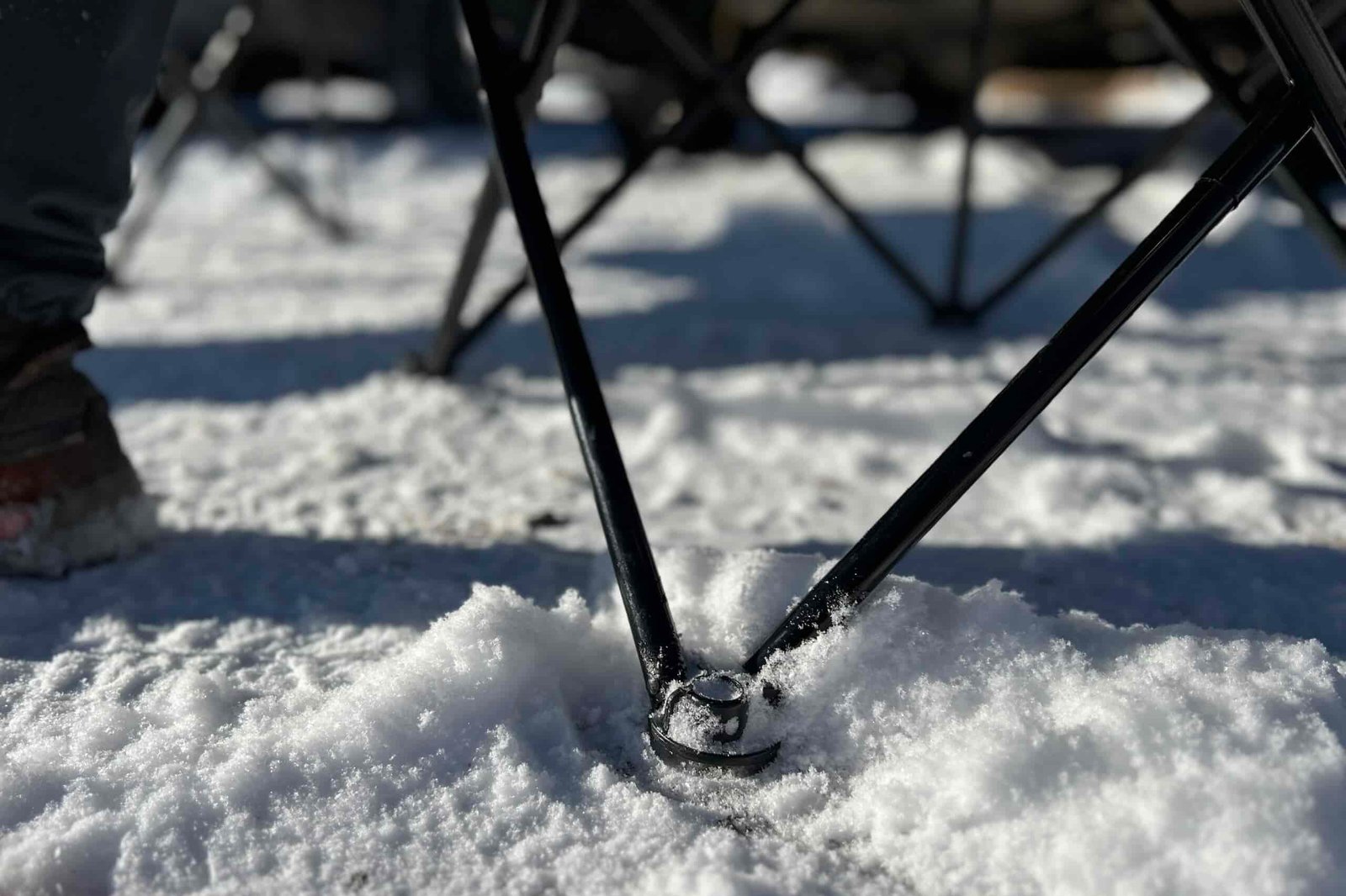 Close up of the feet and legs of a camping chair sitting on snowy ground.