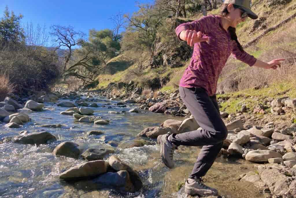 Women jumping across a creek wearing Keen hiking shoes.