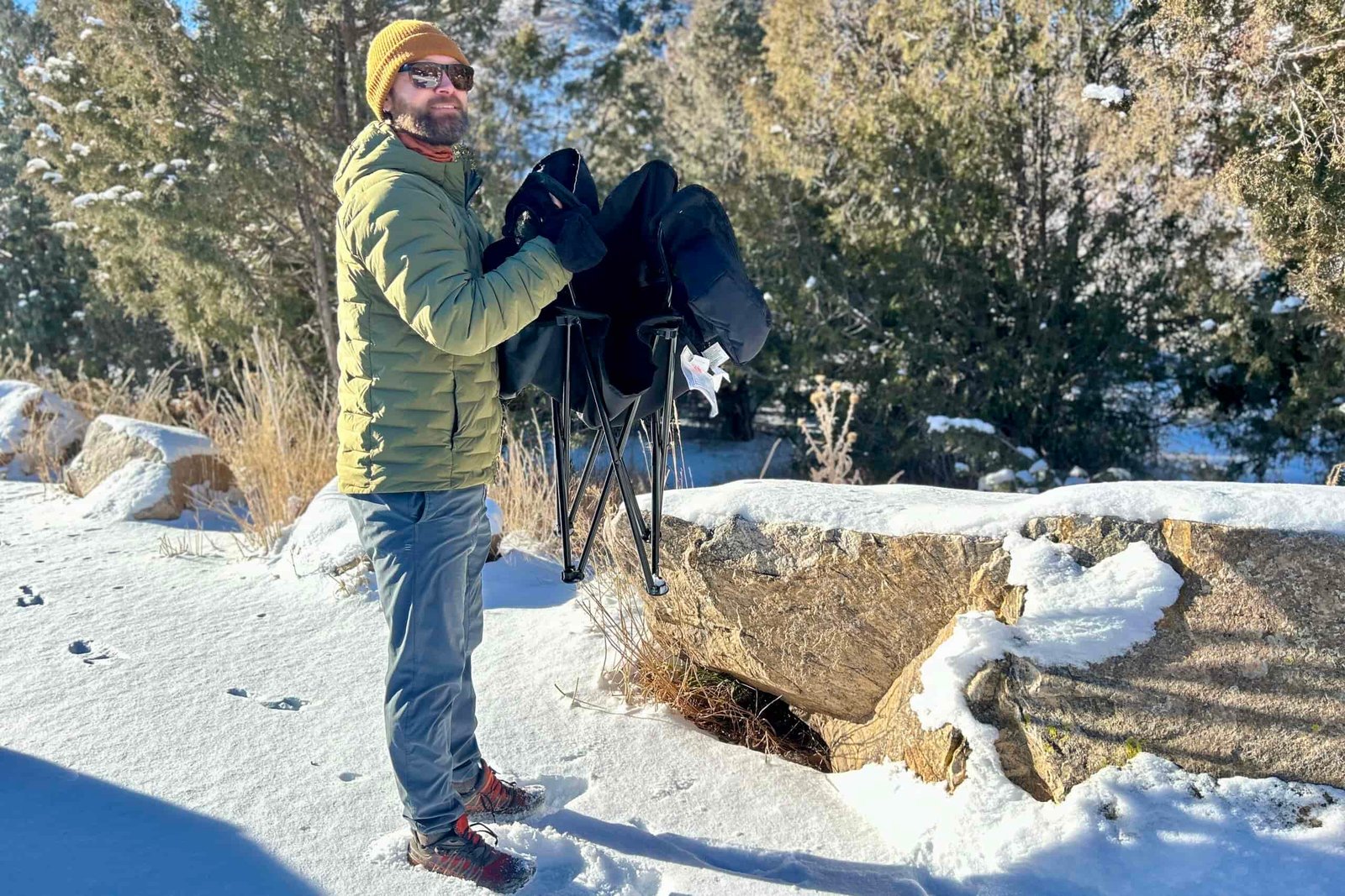 A man standing in a snowy place collapses a camping chair.
