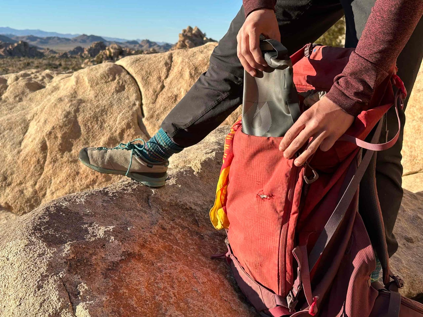 Close up of a hiker loading the HydraPak Seeker water bag into a red backpacking backpack. She is standing on a granite boulder in Joshua Tree National Park.