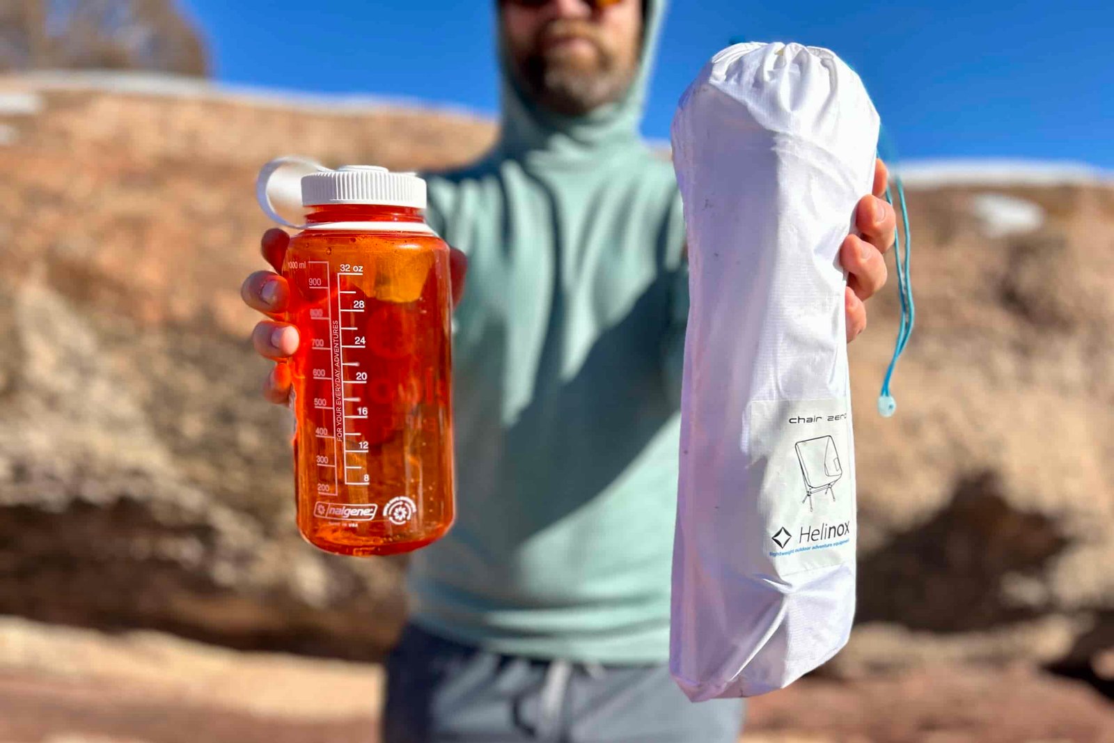 A person holds out a small camping chair in its drawstring bag next to a Nalgene for size reference.