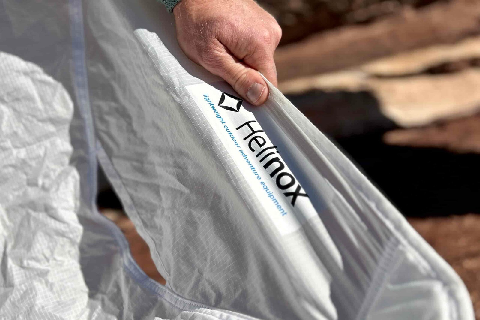 Close up of a hand holding onto the thin white fabric of a camping chair with the logo visible.