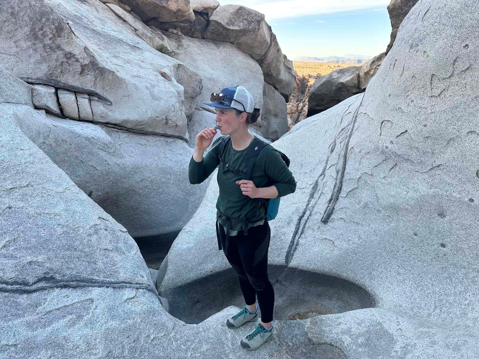 A hiker drinks from a hydration hose while standing in a water-carved granite canyon in the desert.