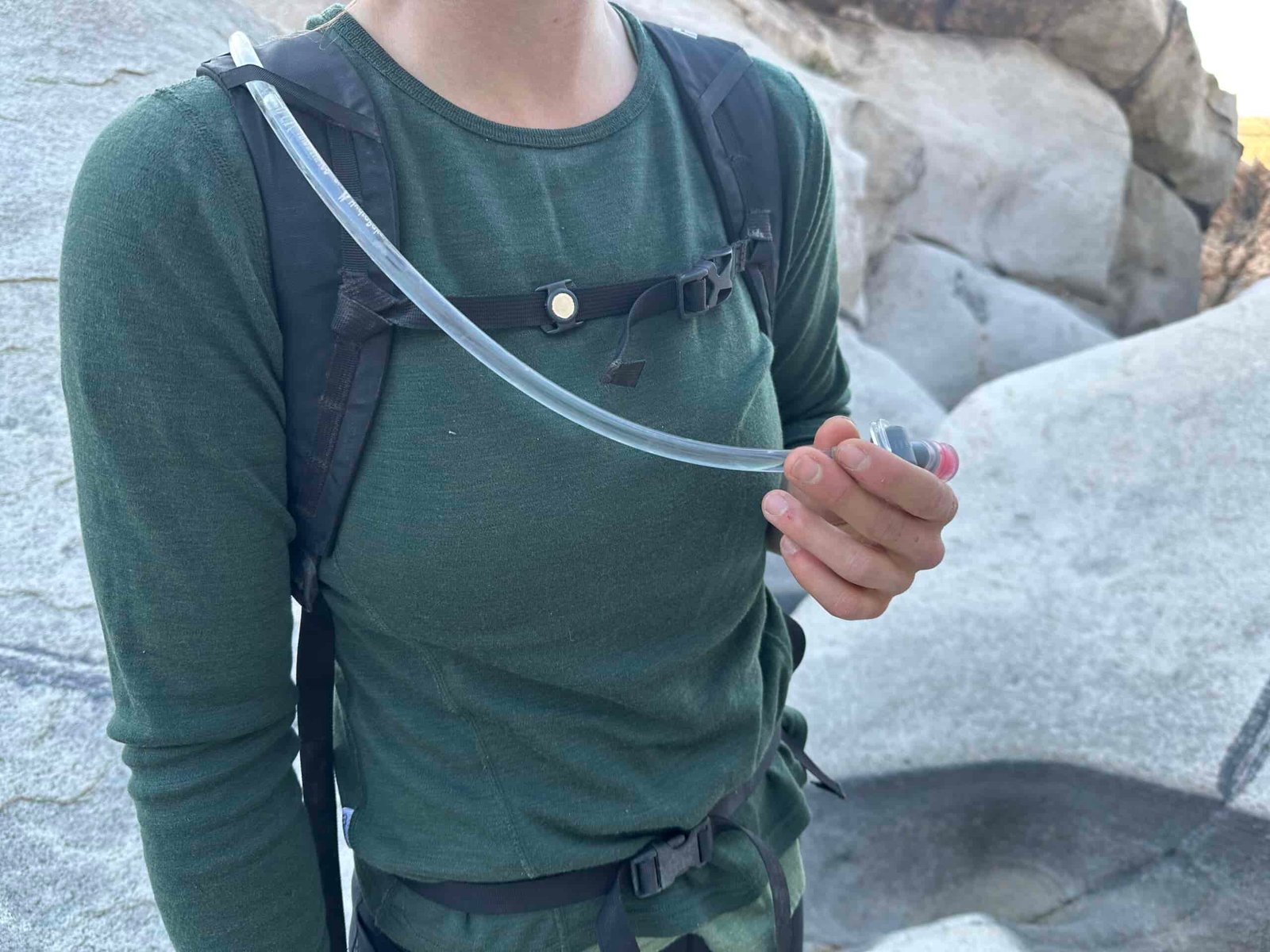 Close up photo of a hiker's chest showing the sternum strap magnet that secures the hydration hose while hiking.