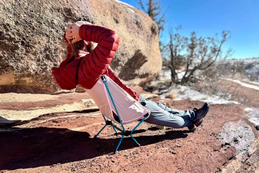 A man relaxes with his legs out and hands behind his head on a small backpacking chair.