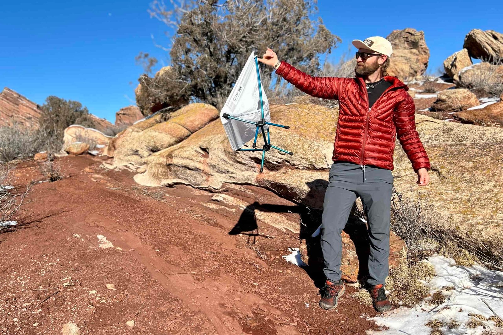 A man holds out a small backpacking chair with one pinky in a desert setting.
