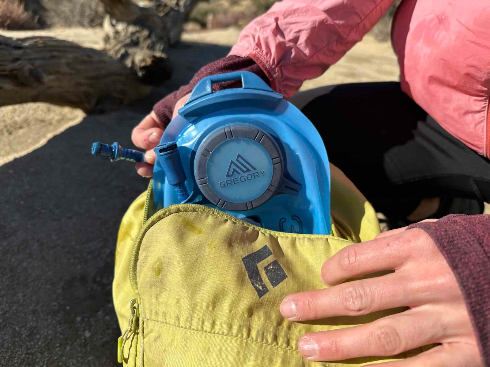 A close up image of a hiker reloading a hydration bladder back into her backpack, showing the hose quick release near the top of the bladder.