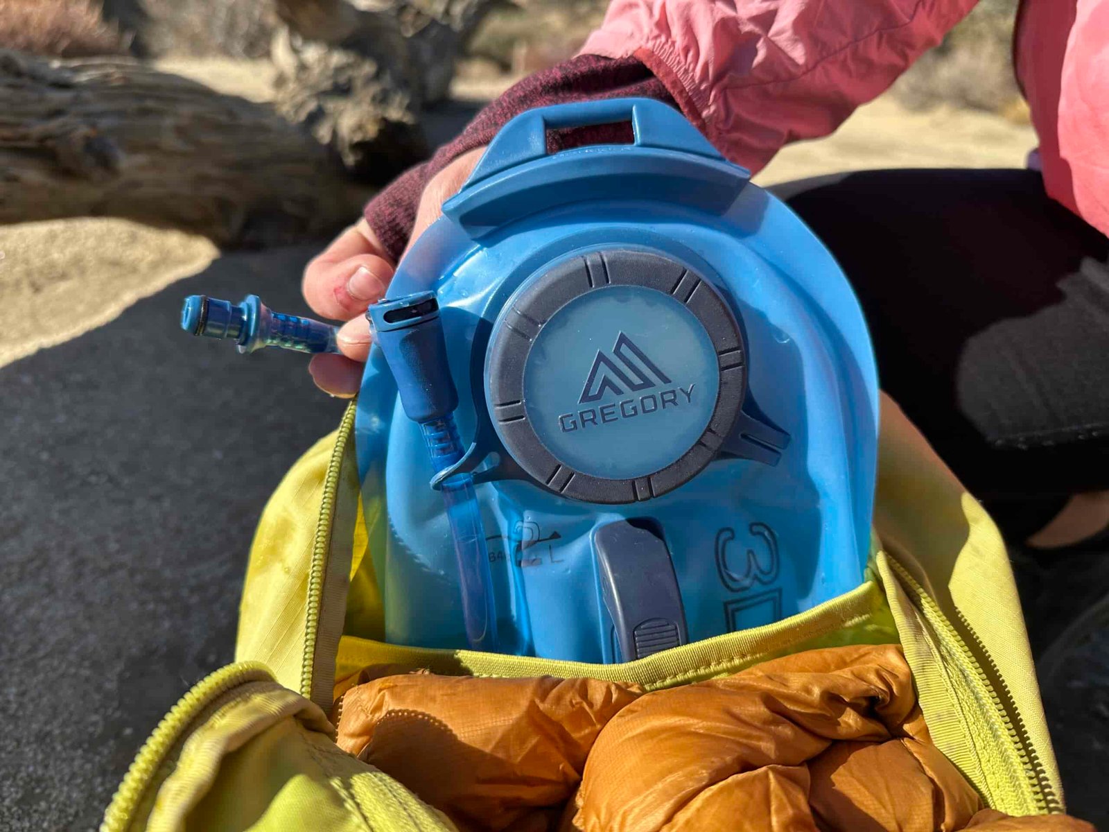 A close up image of a hiker re-loading a Gregory 3D Hydro Reservoir back into the hydration sleeve of a small day pack.