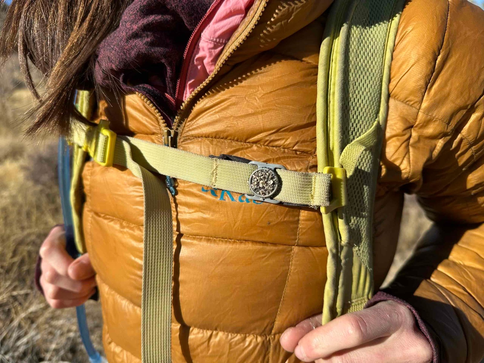 A close-up image showing sand sticking to the sternum strap magnet on a hiker's backpack.