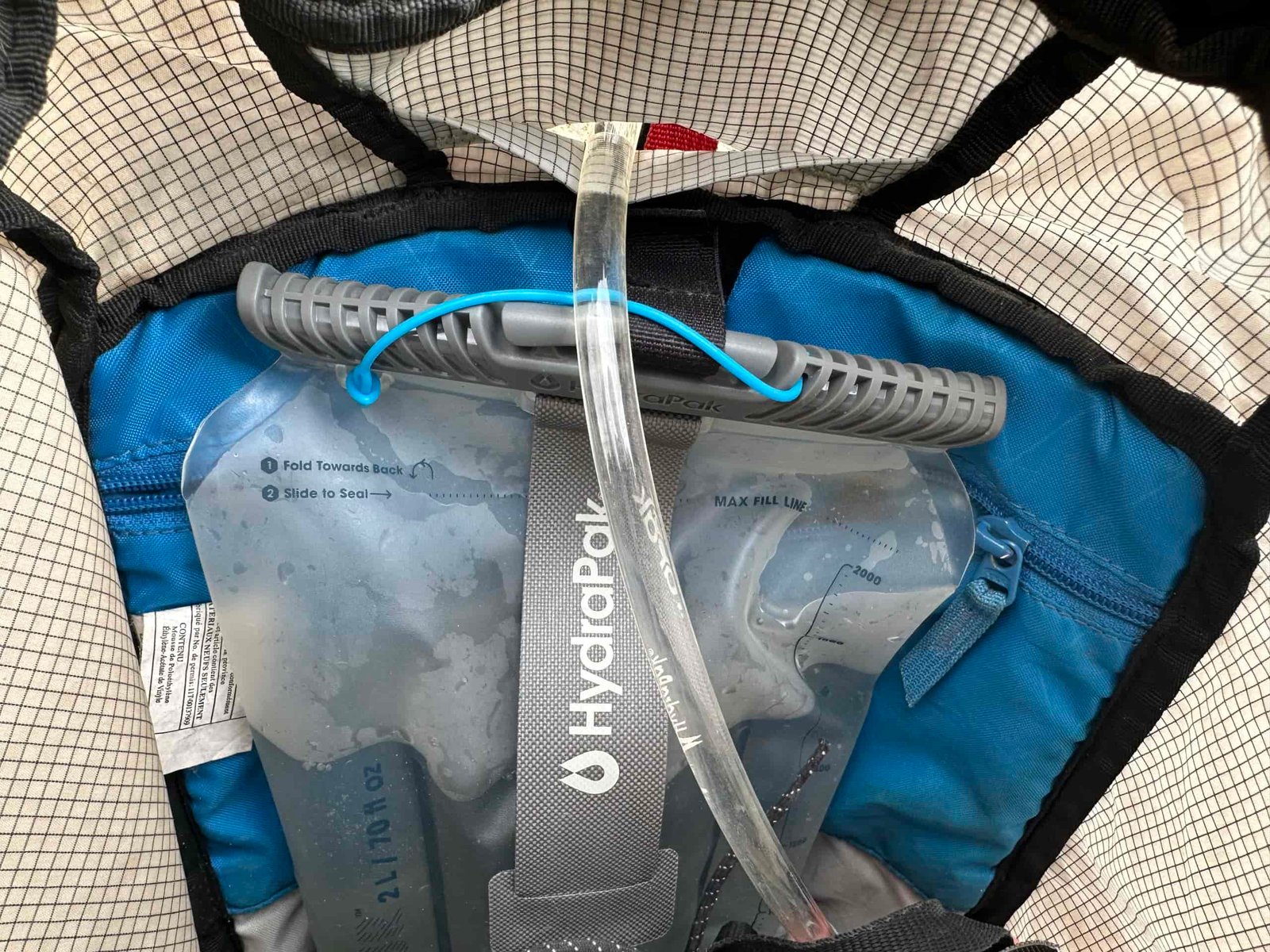 Inside of a backpack showing the HydraPak Contour suspended by a velcro strap, with the hydration hose running out of a hole in the backpack.