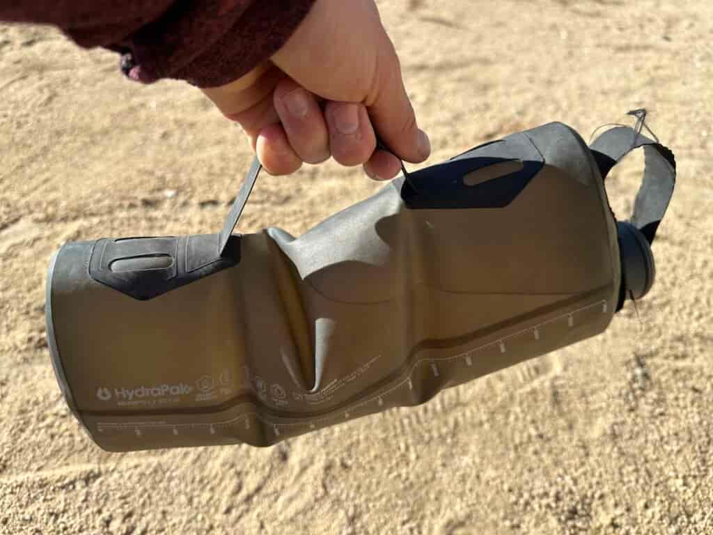 Close-up photo of a hand holding the handle on the side of the HydraPak Seeker water bag. The bag is full of water.