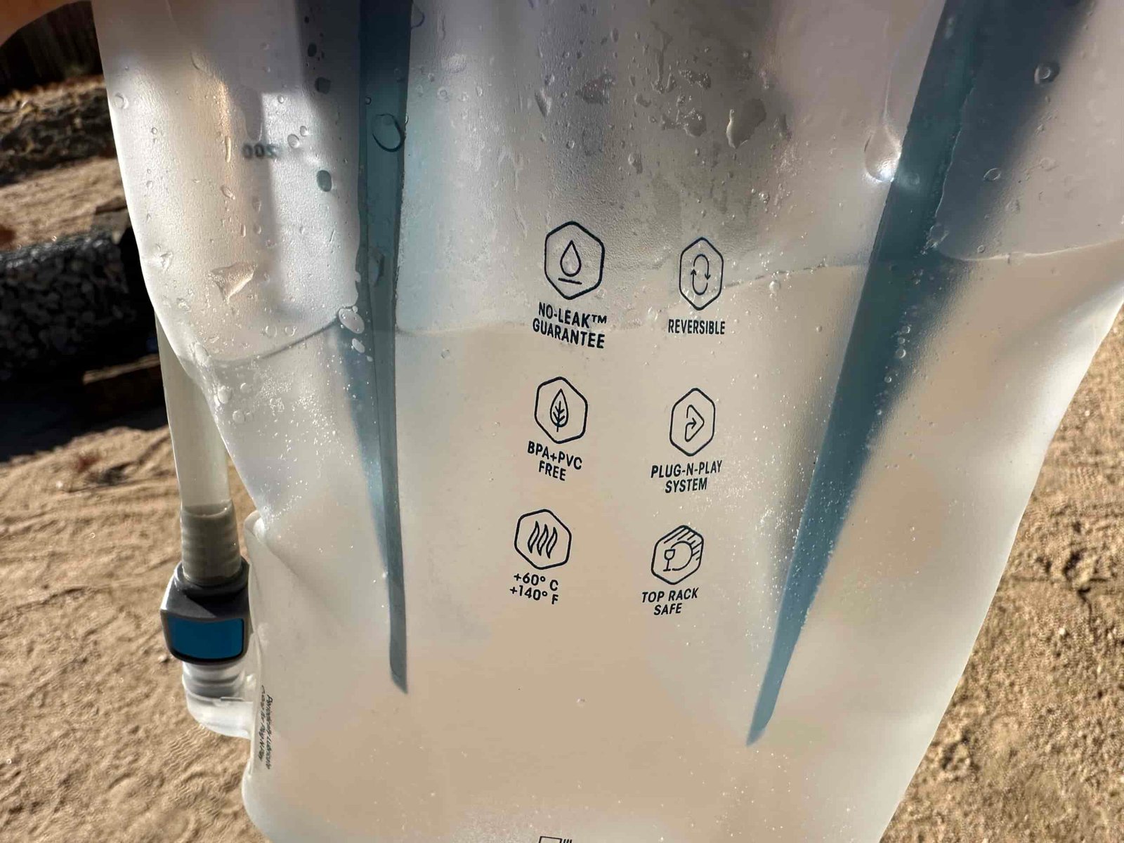 A close-up of the HydraPak Contour, with some water inside. On the bladder are words that read "No leak Guarantee," "Reversible," "BPA +PVC Free," "Plug-n-play system," "+60C +140F," "Top Rack Safe."