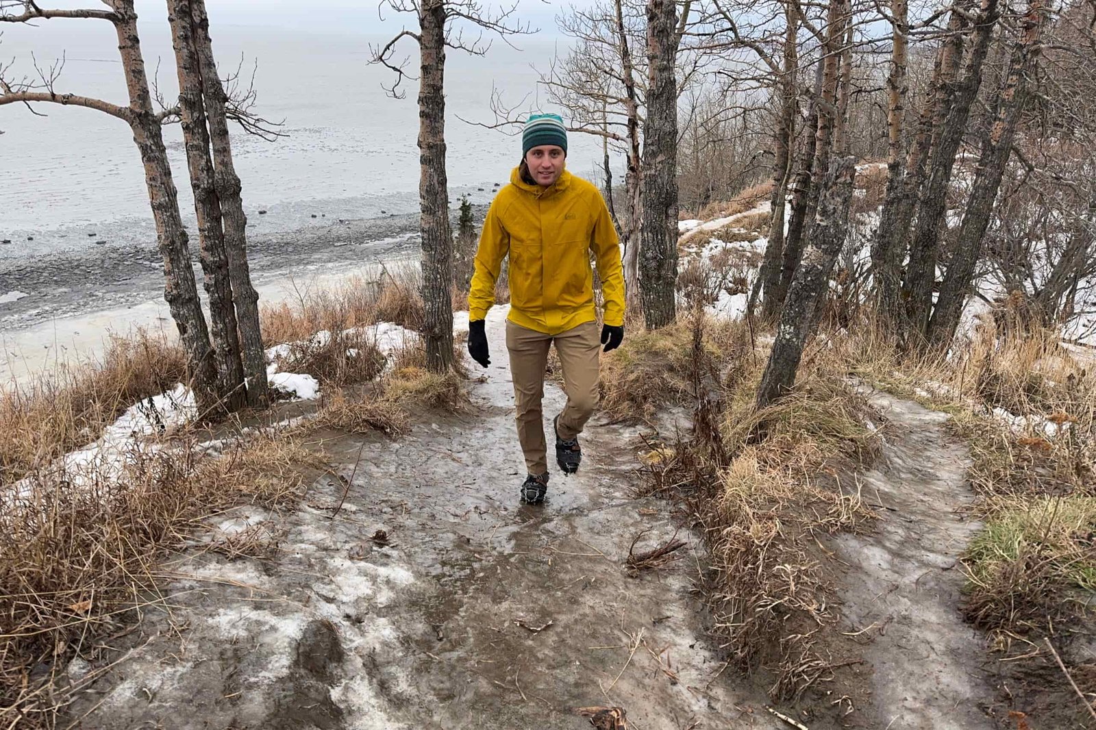 A man in a yellow rain jacket walks up an icy trail.