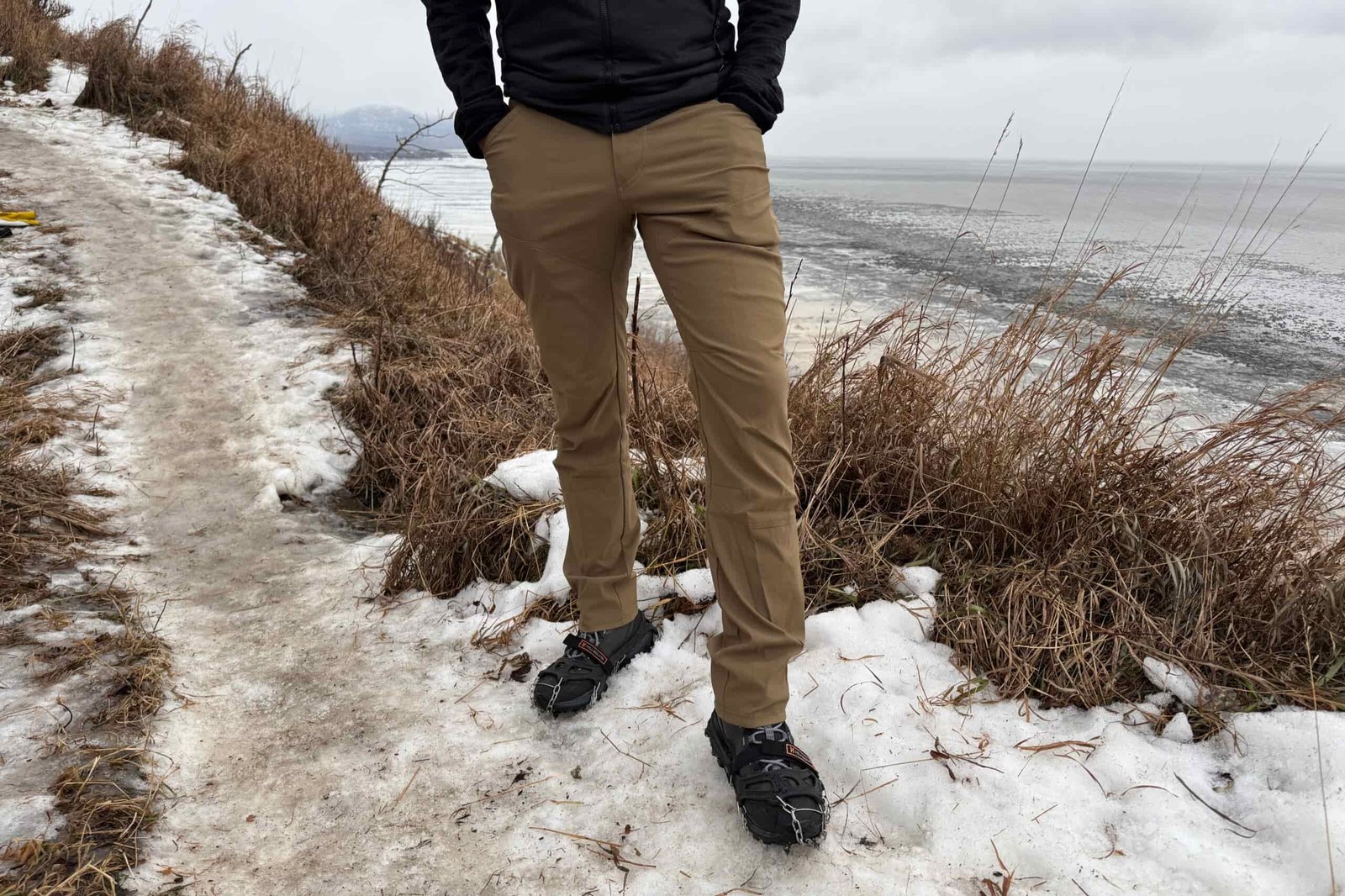 A closeup of pants worn on an icy trail with the coast in the background.