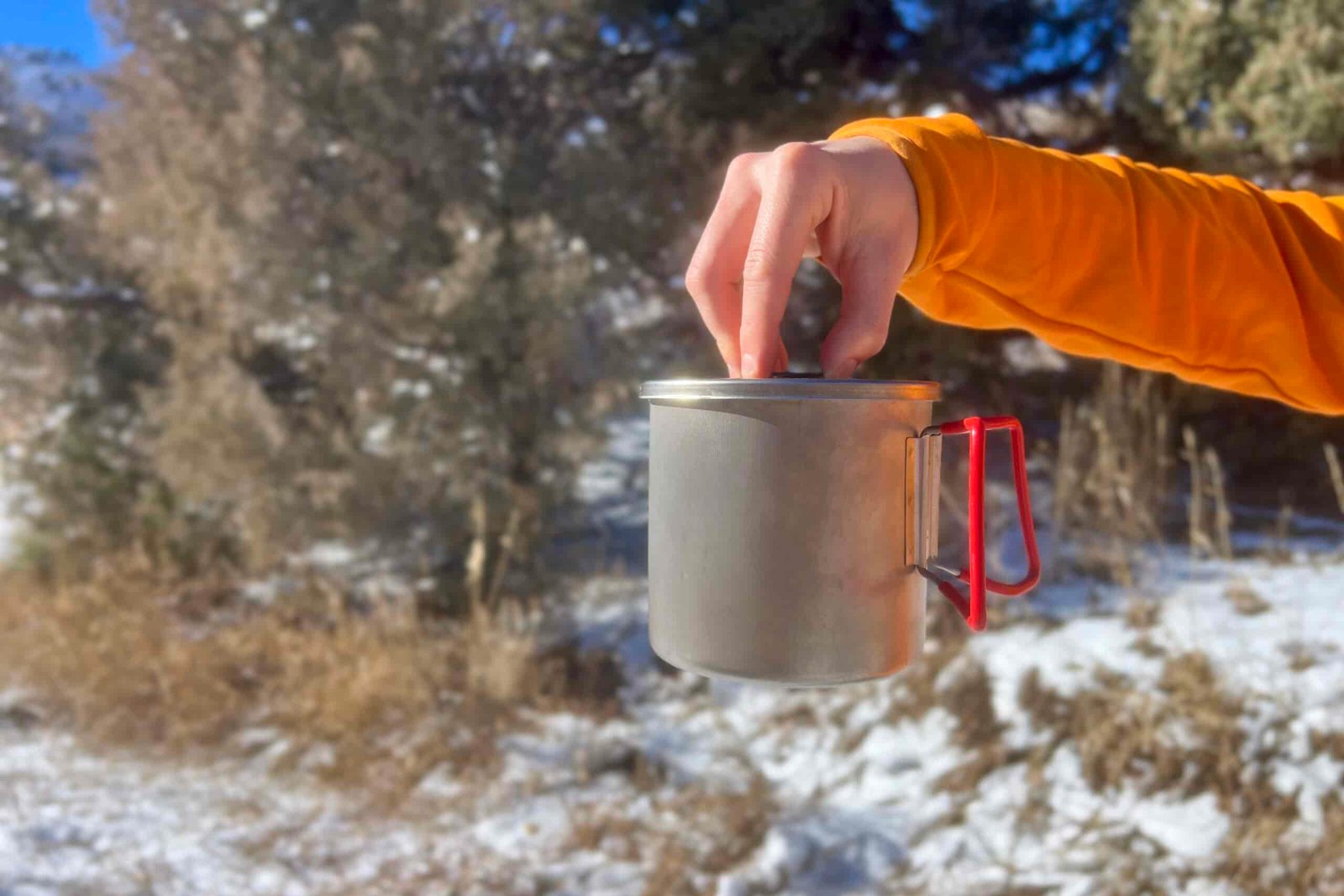 A hand holding the Evernew pasta pot from the lid with a snow background.