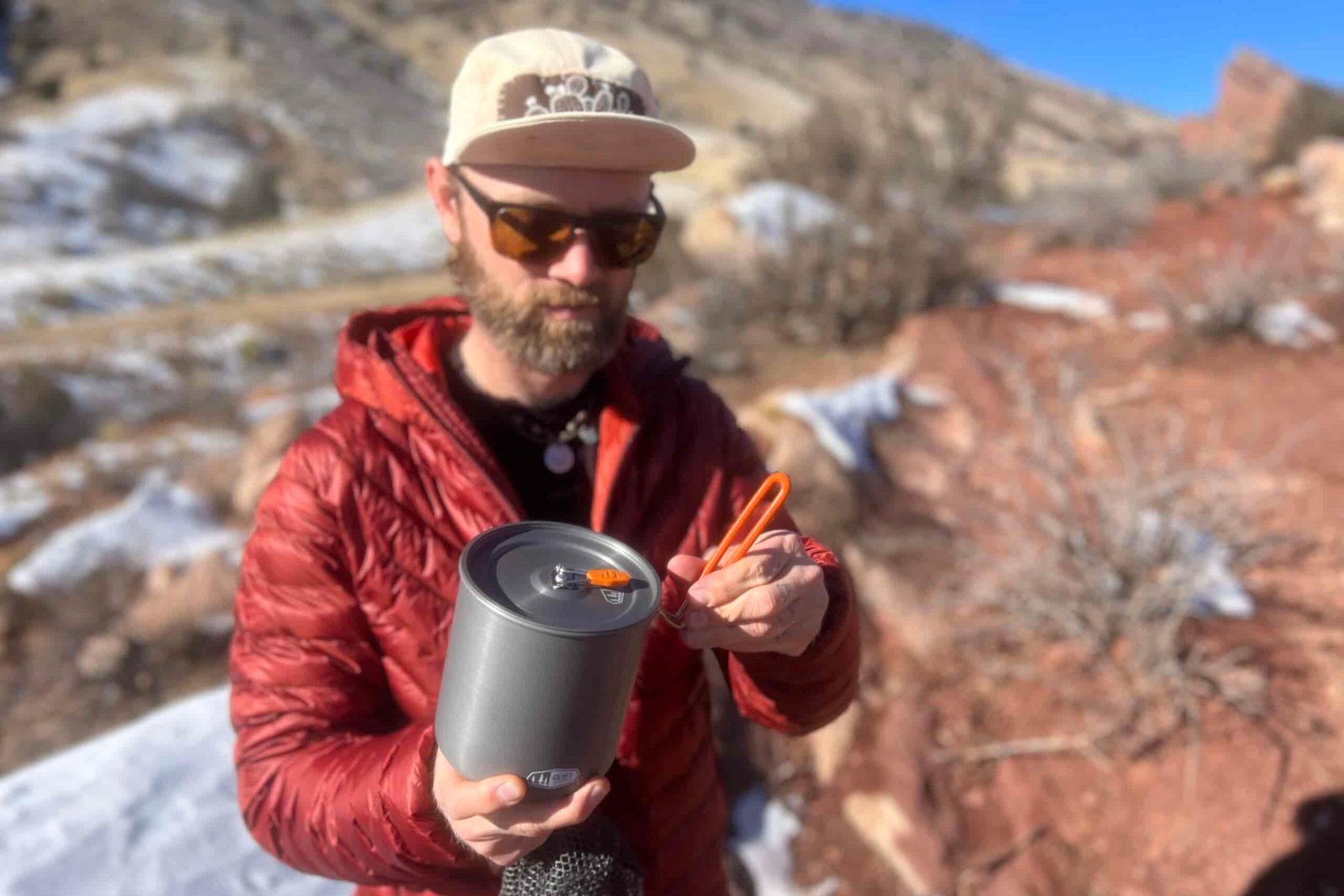 A hiker hinges the handle of the gsi halulite boiler with red rock formations in the background.