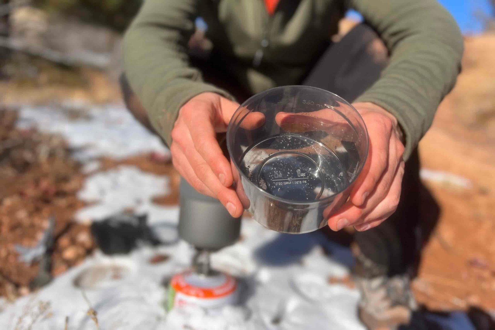 A hiker shows the plastic cup of the msr trail mini solo to the camera against a snowy background.