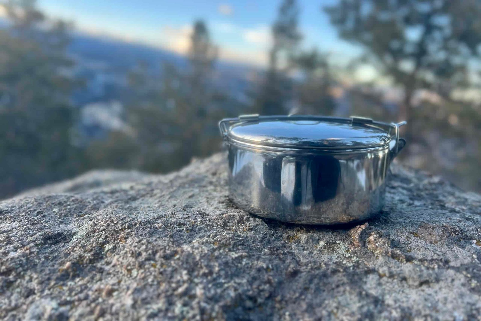 A steel backpacking pot with a foldable handle sitting on a rock